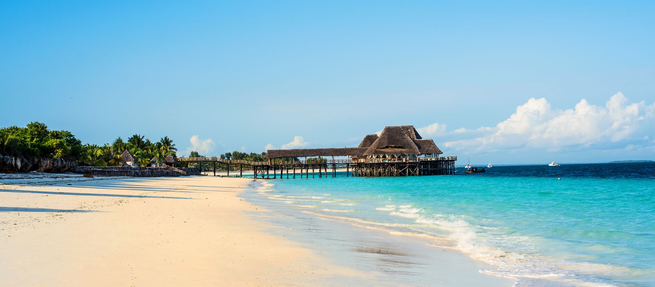 A white-sand beach with a thatched jetty in the distance